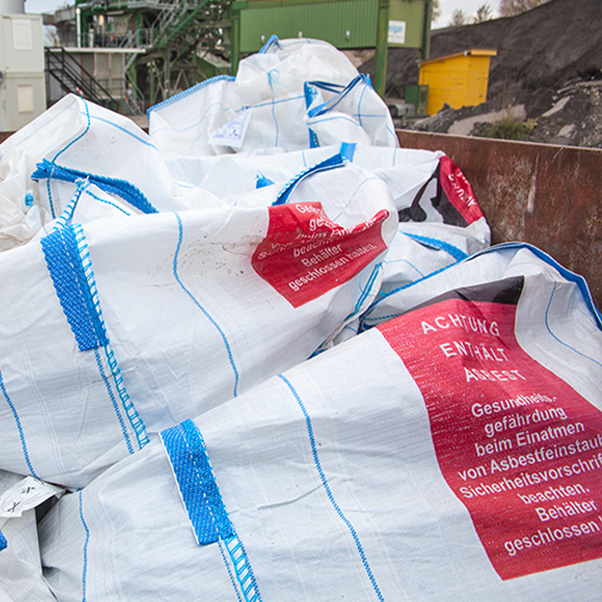 Große weiße Säcke mit blauen Riemen und roten Warnhinweisen enthalten Asbestabfälle.