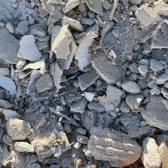 Nahaufnahme von verstreuten, unebenen grauen Felsen und Steinen auf unebenem Gelände, beleuchtet durch natürliches Sonnenlicht.