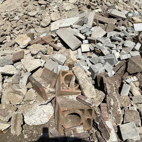 Ein Haufen aus gemischtem Schutt und Trümmern, darunter zerbrochene Ziegel und Betonblöcke, im hellen Sonnenlicht.