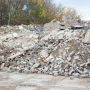 Ein Haufen Schutt und zerbrochene Betonblöcke im Freien mit Bäumen im Hintergrund.