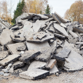 Haufen zerbrochener Betonplatten mit Bäumen im Hintergrund unter einem bewölkten Himmel.