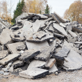 Haufen zerbrochener Betonplatten mit Bäumen im Hintergrund unter einem bewölkten Himmel.