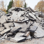 Haufen zerbrochener Betonplatten mit Bäumen im Hintergrund unter einem bewölkten Himmel.