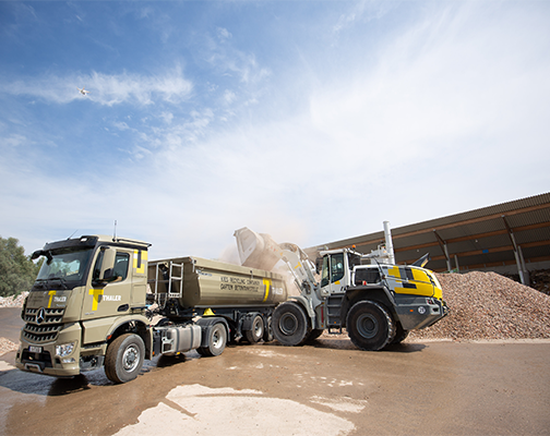 LKW und Lader arbeiten auf einer Baustelle und transportieren Kies unter einem klaren blauen Himmel.