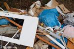 Ein Haufen gemischten Mülls, darunter blaue Säcke, Holzbretter und verschiedene im Freien verstreute Abfälle.