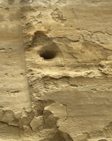 Eine Nahaufnahme einer rauen, verwitterten Steinoberfläche mit einem kleinen Loch, mit verschiedenen Texturen und Schichten.