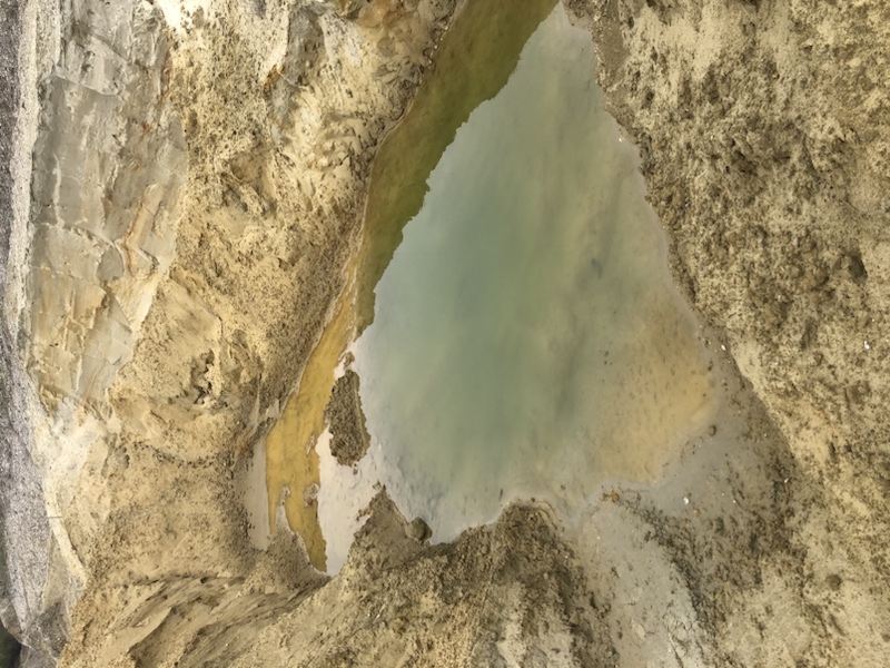 Ein schmaler, schlammiger, mit Wasser gefüllter Graben verläuft unter einem bewölkten Himmel durch eine sandige, ausgehöhlte Landschaft.