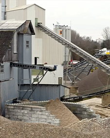 Eine Kiesaufbereitungsanlage mit Förderbändern und Kieshaufen unter bewölktem Himmel.
